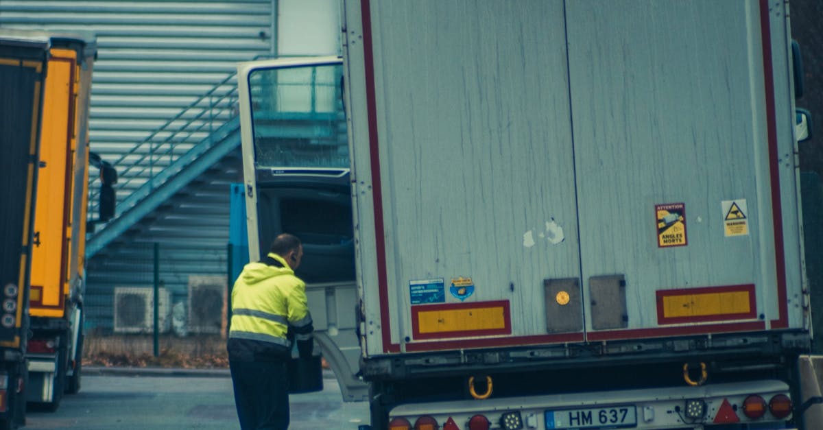 A truck driver in high-visibility gear unloading cargo at an industrial facility.