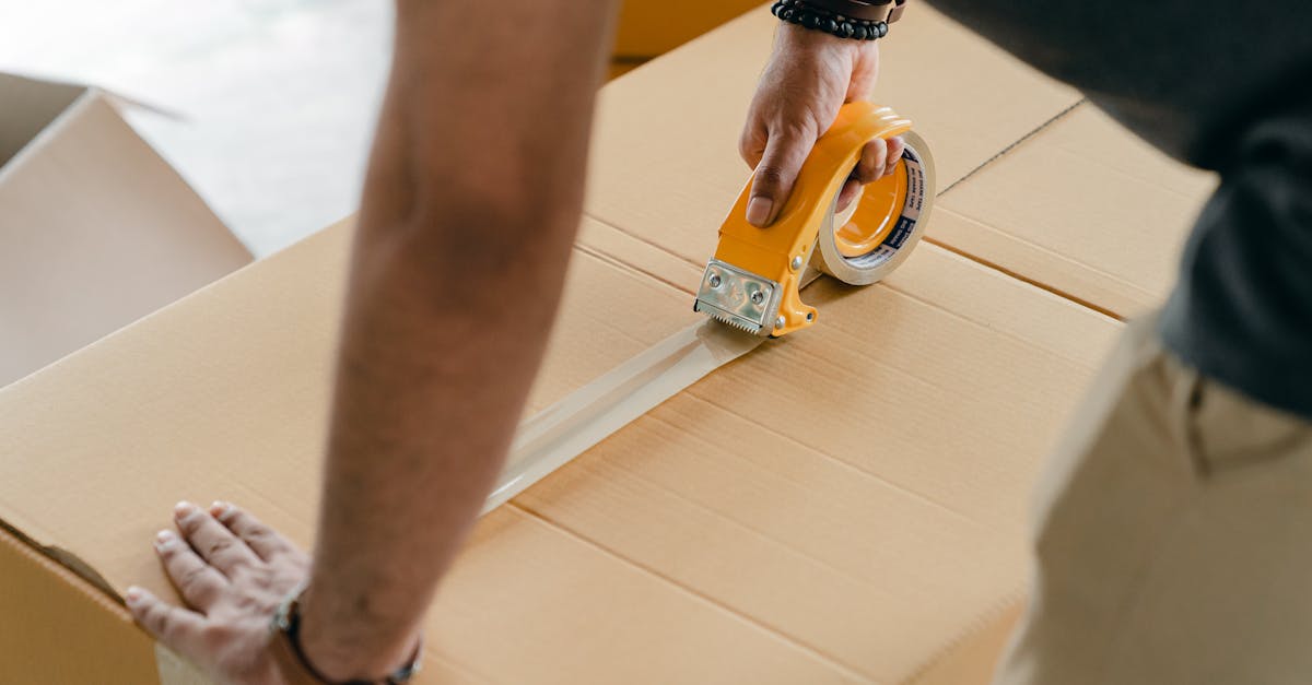 Man using packing tape to seal a cardboard box indoors. Ideal for moving or shipping concepts.