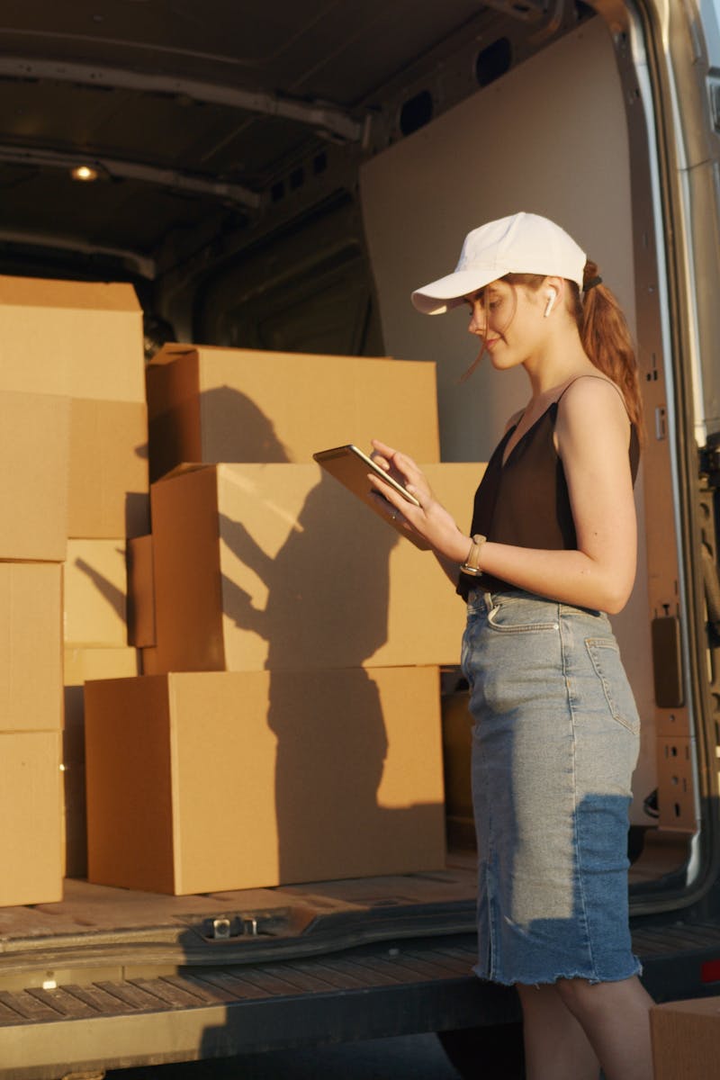 Young female courier organizing package delivery beside an open delivery van at sunset.